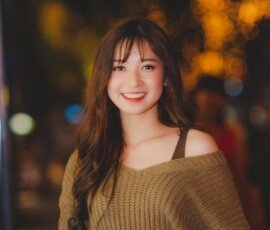 Warm outdoor portrait used as a sample transformation on MixPlay. Smiling woman posing outdoors in a warm autumn sweater with glowing background lights.